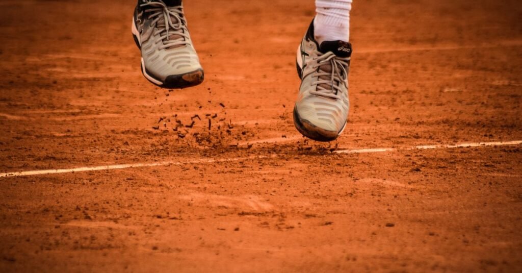 Close-up of an athlete's shoes mid-jump on a clay tennis court.