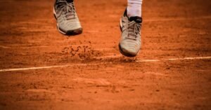 Close-up of an athlete's shoes mid-jump on a clay tennis court.