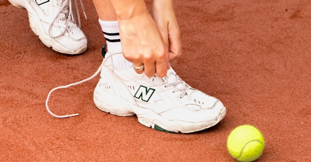 Close-up of a tennis player tying their shoes on clay court with ball nearby.